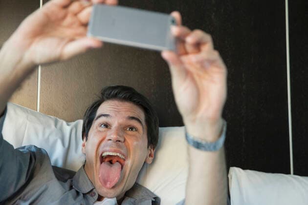 Man using smartphone to take a selfie, sticking out tongue  Copyright: SigridxOlsson B77504433