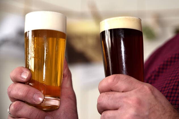 Zwei Hände halten je ein Bierglas mit Pils und eins mit obergärigem Bier vor unscharfem Hintergrund. Zwei Biergläser mit hellem und dunklem Bier, Schwerte Nordrhein-Westfalen Deutschland