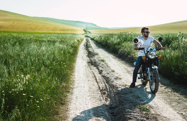 young man parks his motorcycle on the green field road to contemplate Spain, Andalusia, Seville CR_FAGU191022-208018-01