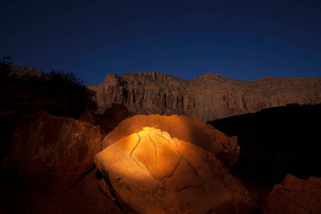 The orange glow of a flashlight illuminates a cracked rock at night United States, Arizona CR_MALI191022B-87084-01
