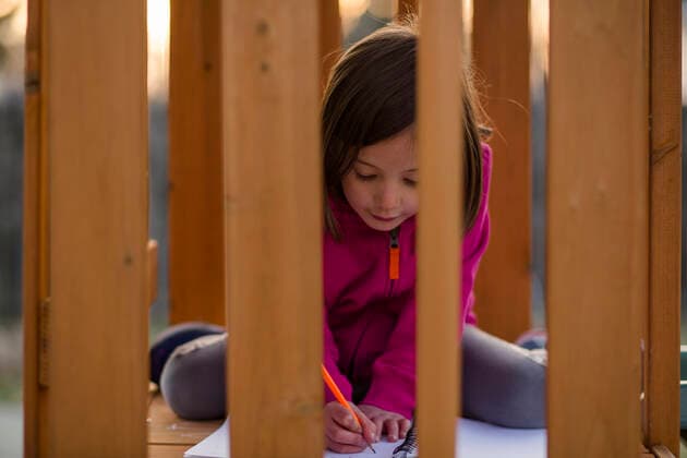 IMAGO Creative: Bildung, Schreiben A little girl sits on playset at sunset writing with paper and pencil United States, Ohio, Columbus CR_RETI190924-153253-01