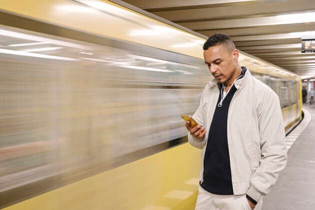 Portrait of man standing in front of driving underground train looking at cell phone, Berlin, Germany model released Symbolfoto  AHSF01125