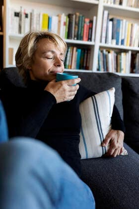 IMAGO Creative: Internationaler Frauenmonat, Gesundheit, Frauen in der Menopause Mature woman relaxing on couch at home drinking from cup model released Symbolfoto property released  VABF02375