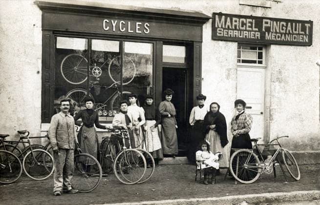 CYCLISME annees 1900 Devanture d un magasin de cycles, Marcel PINGAULT le patron en bleu de travail, des femmes et jeunes filles, une vieille femme, une petite fille et sa poupee. . Photographie anonyme pour une carte postale vers 1907. Credit : Collection IM KHARBINE-TAPABOR. *** CYCLING in the 1900s in front of a bicycle shop, Marcel PINGAULT the boss in work clothes, women and young girls, an old woman, a little girl and her doll Anonymous photograph for a postcard around 1907 Credit Collection IM KHARBINE TAPABOR  KH177074