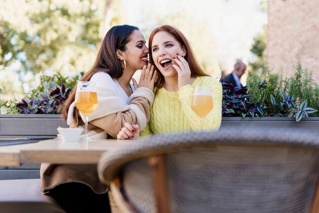 Two female friends whispering outdoors at a coffee shop model released Symbolfoto  ERRF02204