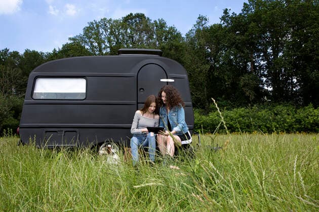 Two best friends sitting on a meadow in front of black caravan using digital tablet model released Symbolfoto property released  PSTF00489