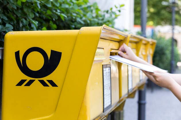 Frau steckt mehrere Brief in einen Briefkasten der Deutschen Post AG *** Woman puts several letters into a mailbox of the Deutsche Post AG