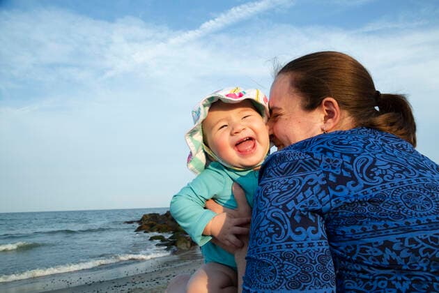 Mother hugs happy smiling baby girl while sitting on beach New Jersey, USA CR_ACZQ191106-207515-01