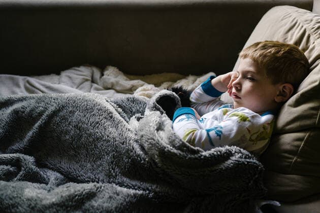 A little boy lies on a couch with a furry blanket. Garden City South, New York, USA CR_FRRU191112-229824-01