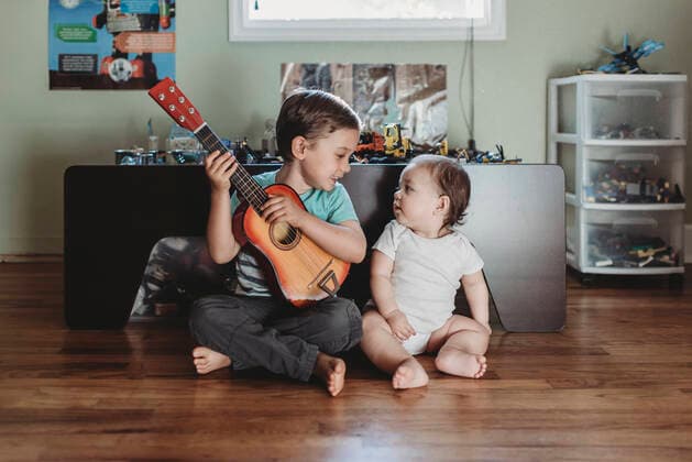 Baby sister and big brother with guitar sitting on hardwood floor La Mesa, CA CR_KESM191114A-213180-01