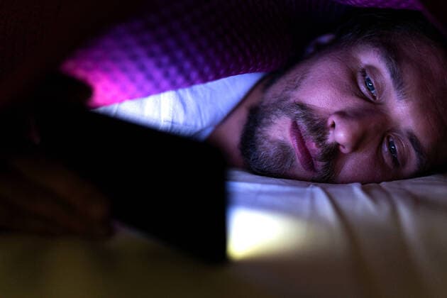 Bearded young man is lying in bed under his blanket looking at phone Wlodawa, Lubelskie, Poland CR_QLKC191113B-234673-01