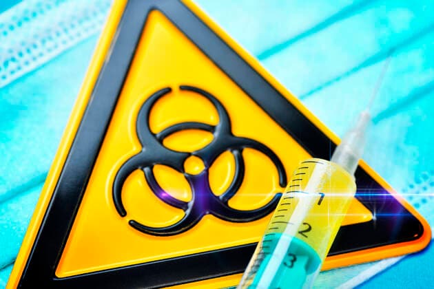 Spritze und BiogefÃ¤hrdungsschild auf einem Mundschutz, Symbolfoto Coronavirus