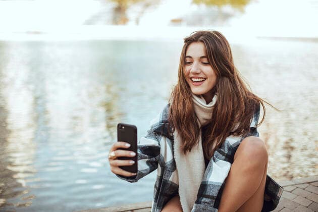 Young brunette woman using smartphone and taking a selfie at lake model released Symbolfoto  ACPF00659