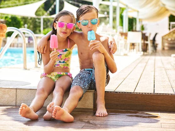 Portrait of little girl and boy with popsicles wearing mirrored sunglasses in front of swimming pool model released Symbolfoto  DIKF00360