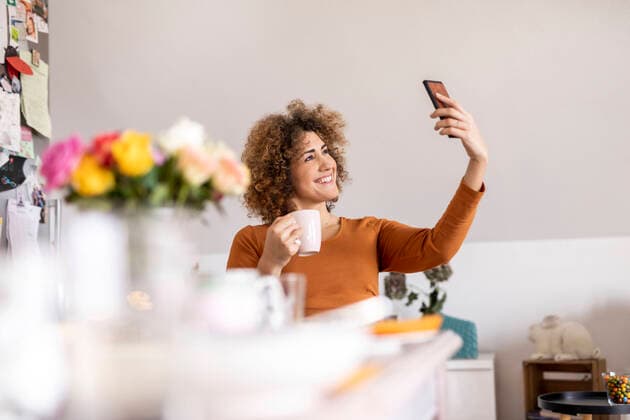 Woman holding coffee cup and taking a selfie at home model released Symbolfoto property released  FMKF06072