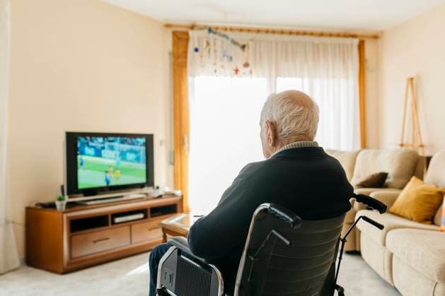 Back view of senior man sitting in wheelchair watching TV at home model released Symbolfoto property released  JRFF03940