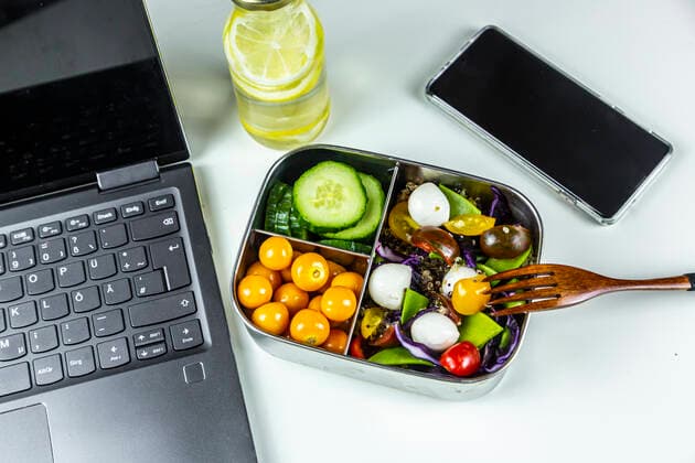 Laptop, smart phone, bottle of lemonade and lunchbox with cucumber slices, winter cherries and quinoa salad (quinoa, cherry tomato, red cabbage, sugar snap peas and mozzarella balls)  SARF04410