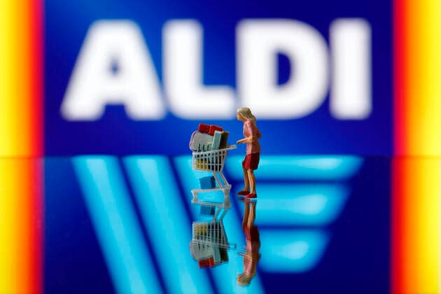 Eine Frau schiebt einen Einkaufswagen vor dem Logo des Konzerns Aldi