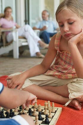 Little girl playing chess with brother at porch while parents sitting in background Girl Playing Chess With Brother At Porch  Copyright: xmoodboardx 10007294