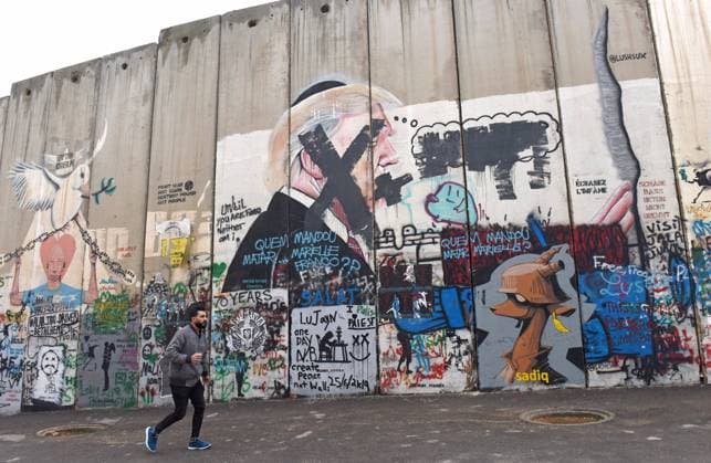 A Palestinian walks past graffiti of U.S. President Donald Trump, that s been vandalized, on the Israeli separation wall in Bethlehem, West Bank, on Wednesday, January 29, 2020. Palestinians say Trump s Deal of the Century for Middle East peace highly favors the Israeli Jewish state.  JER2020012905 DEBBIExHILL