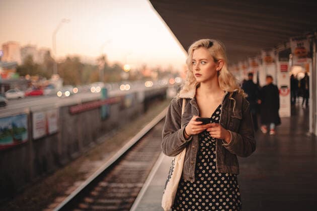Young thoughtful woman using smart phone while waiting for train CR_DMBE191216A-249778-01