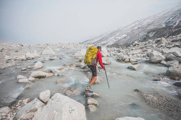 Backpacker uses large boulders to cross river next to glacier. Pemberton, BC, Canada CR_JDIP200102-245479-01