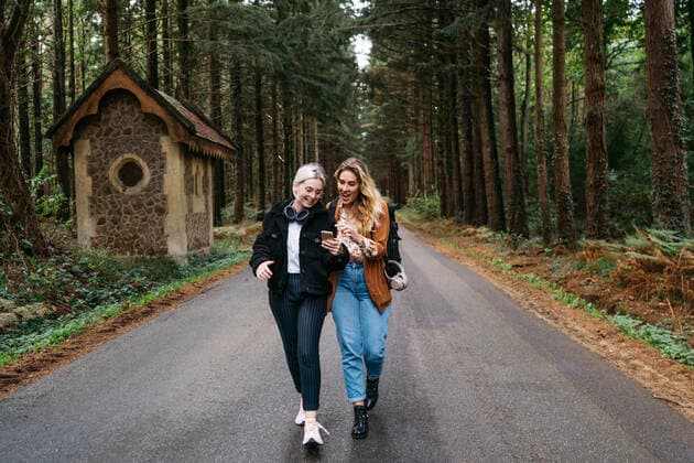 Two women walking down the road looking at their phone and laughing Sarthe, France CR_MIVE191211-230591-01