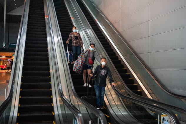 31.01.2020, Singapur, Republik Singapur, Asien - Angekommene Flugreisende auf einer Rolltreppe unterwegs zum U-Bahnhof am Flughafen Changi. Sie tragen Atemschutzmasken, um sich vor einer Ansteckung mit dem Coronavirus zu schuetzen.