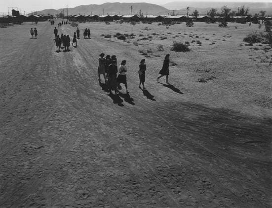 Interned Japanese Americans, mostly women, holding books, walking on a dirt road, within the guarded fences of the Manzanar Relocation Center during World War II. Master photographer Ansel Adams captured the bleak landscape of the isolated internment camp Courtesy Everett Collection PUBLICATIONXNOTxINxCANxCHNxFRAxITAxJPNxNORxPOLxRUSxESPxUKxUSA Copyright: xCourtesyxEverettxCollectionx HISL017 EC116