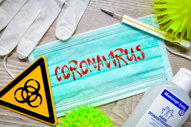 FOTOMONTAGE, Mundschutz mit Coronavirus-Schriftzug, BiogefÃ¤hrdungsschild, Schutzhandschuhe, Fieberthermometer und Desinfektionsmittel auf einem Tisch