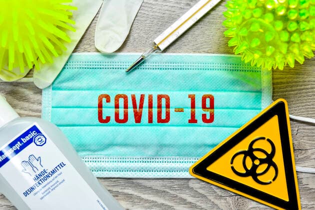 FOTOMONTAGE, Mundschutz mit Schriftzug Covid-19, BiogefÃ¤hrdungsschild, Schutzhandschuhe, Fieberthermometer und Desinfektionsmittel auf einem Tisch, Symbolfoto Coronavirus