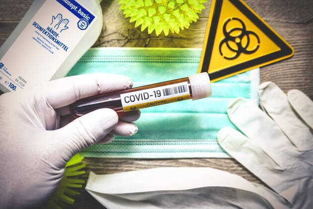 Hand im Latexhandschuh hÃ¤lt BlutentnahmerÃ¶hrchen vor einem Mundschutz, Symbolfoto Coronavirus
