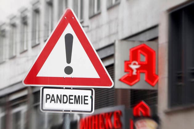 (Fotomontage) Symbolbild zur Ausbreitung des Coronavirus und der öffentliche Umgang mit der Krankheit: Verkehrsschild Achtung Gefahr mit Zusatz Pandemie vor dem Logo einer Apotheke in Frankfurt, Hessen, Deutschland