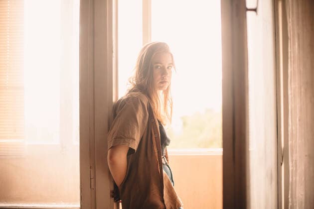 Young woman leaning on balcony doorway at home in summer CR_DMBE200115-273233-01