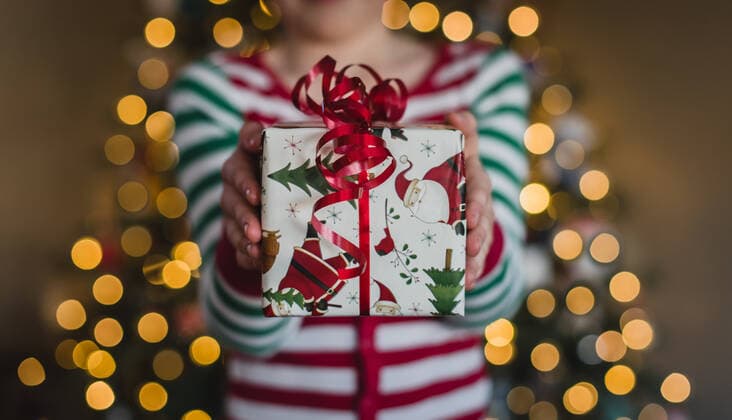 Child in pyjamas holding Christmas gift in front of lights on tree. Kingston, ON, Canada ,model released, Symbolfoto CR_DOHO200115B-281169-01