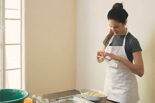 Woman in apron photographing Challah bread with smart phone on table against wall Los Angeles, CA, United States ,model released, Symbolfoto CR_JAJEES200212-305466-01