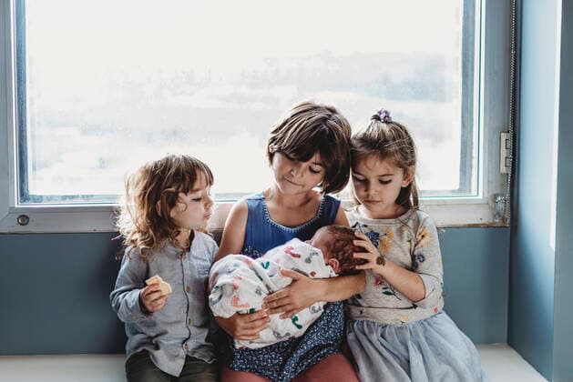 Front view of three siblings holding newborn brother against window San Diego, CA, United States ,model released, Symbolfoto CR_KESM200220-261055-01