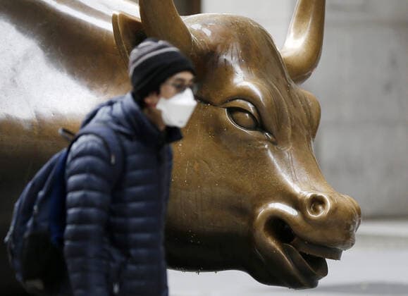 A man wearing a protective face mask walks by the Walk Street Statue of the Charging Bull after the opening bell on Wall Street in New York City on Friday, March 20, 2020. The New York Stock Exchange will close down the floor and will move temporarily to fully electronic trading on Monday, March 23 due to the Coronavirus pandemic.  NYP20200320154 JOHNxANGELILLO
