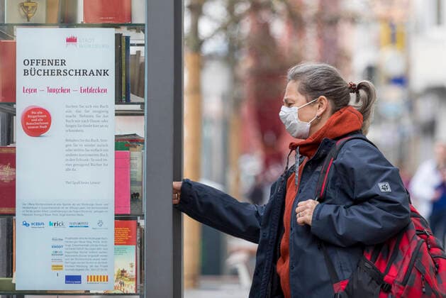 Wuerzburg, City 20.03.2020, Coronavirus: Buecher ausleihen in Zeiten Coronas Bild: Eine Frau steht am Freitag vor einem offenen Bücherschrank in der Würzburger Innenstadt. Wegen der Coronakrise hat sie eine Schutzmaske auf. Bayern, Coronavirus, COVID-19, Deutschland, Franken, Katastrophenfall, Konsum, Krankheiten, Mainfranken, Schutzmaßnahmen, Würzburg, Vorsorge, Schutz, Copyright: HMBxMediax xPattyxVarasano