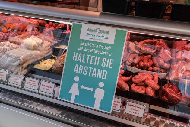 DEU, Deutschland, Nordrhein-Westfalen, Münster, 21.03.2020: Anfang des 20. Jahrhunderts war der Wochenmarkt Münster vom Prinzipalmarkt auf den Domplatz umgezogen. Wegen der Corona Ansteckungsgefahr wurde der Wochenmarkt entzerrt, damit zwischen Ständen Freiflächen für wartende Kunden entstehen. Einige Marktstände stehen deshalb am Prinzipalmarkt und am Michaelisplatz werden Stände aufgebaut. Abstandsregeln wurden von den Kunden beachtet. Schild Halten Sie Abstand