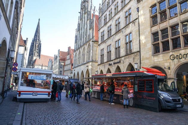 DEU, Deutschland, Nordrhein-Westfalen, Münster, 21.03.2020: Anfang des 20. Jahrhunderts war der Wochenmarkt Münster vom Prinzipalmarkt auf den Domplatz umgezogen. Wegen der Corona Ansteckungsgefahr wurde der Wochenmarkt entzerrt, damit zwischen Ständen Freiflächen für wartende Kunden entstehen. Einige Marktstände stehen deshalb am Prinzipalmarkt und am Michaelisplatz werden Stände aufgebaut. Abstandsregeln wurden von den Kunden beachtet.