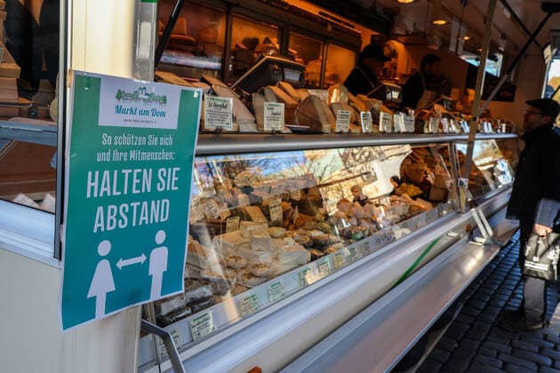 DEU, Deutschland, Nordrhein-Westfalen, Münster, 21.03.2020: Anfang des 20. Jahrhunderts war der Wochenmarkt Münster vom Prinzipalmarkt auf den Domplatz umgezogen. Wegen der Corona Ansteckungsgefahr wurde der Wochenmarkt entzerrt, damit zwischen Ständen Freiflächen für wartende Kunden entstehen. Einige Marktstände stehen deshalb am Prinzipalmarkt und am Michaelisplatz werden Stände aufgebaut. Abstandsregeln wurden von den Kunden beachtet. Schild Halten Sie Abstand