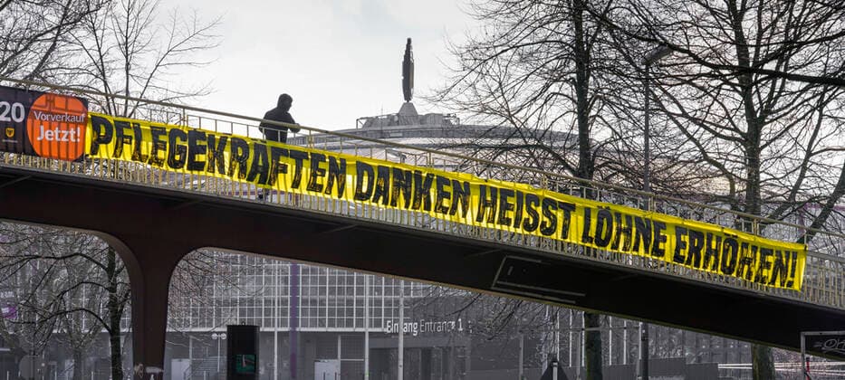 Dortmund, 21.3.2020: Im Zusammenhang mit der Personalbelastung in der Pflege während der Coronakrise hängt ein Banner mit der Forderung zur Lohnerhöhung für Pflegekräfte an einer Fussgängerbrücke über dem Rheinlanddamm (Bundesstrasse 1) im Stadtbereich von Dortmund.