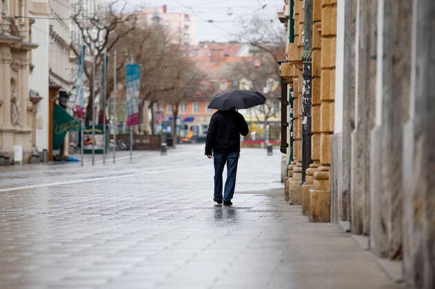 Graz 21.03.2020, Innenstadt, Graz, AUT, Coronavirus in Oesterreich, Die Oesterreichische Bundesregierung hat die verhaengten Ausgangsbeschraenkungen bis zum 13. April 2020 verlaengert. Im Bild ein Spaziergaenger mit Regenschirm im Regen in der herrengasse in Graz A stroller in the rain in the Herrengasse in Graz. The Austrian government extended the measures and laws to contain and spread dthe Corona Virus pandemic until April 13 2020., in Graz, Austria on 2020 03 21.