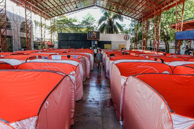(200323) -- MANILA, March 23, 2020 -- A man walks between modular tents set up for street dwellers to stop the further spread of COVID-19 at a sheltered basketball court in Manila, the Philippines on March 23, 2020. The Philippine health authorities confirmed on Sunday 73 new cases of COVID-19 in the country, bringing the total number of people sick with the highly contagious disease to 380. ) PHILIPPINES-MANILA-COVID-19-MODULAR TENTS ROUELLExUMALI 
