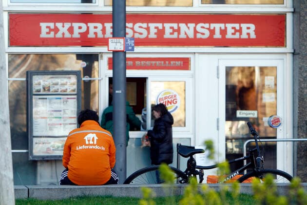 Fahrradkurier vom Internet Portal Lieferando wartet vor einem Expressfenster einer Burger King Filiale auf eine Bestellung zum Ausliefern an einen Kunden in der Innenstadt Mannheim aus, Hessen, Deutschland