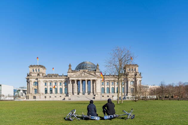 23.03.2020, Berlin, Deutschland, GER - Impressionen aus Berlin während der Ausgangsbeschränkung: Ein Pärchen sitzt gemeinsam vor der menschenleeren Wiese am Reichstag.