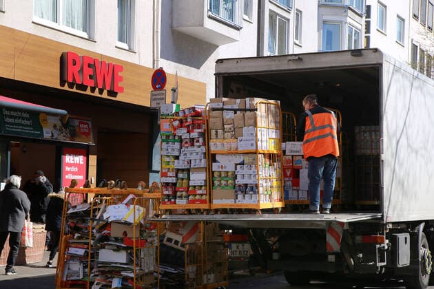 24.03. 2020 Dortmund, NRW Die Coronakrise verschärft sich. Die Bundes- und Landesregierungen erlassen umfasssenden Richtlinien. In allen Lebensbereichen erleben auch die Dortmunder Bürger starke Einschränkungen.. Während die Kunden in einer Schlange vor einer Filiale von REWE stehen bis sie eingelassen werden liefert ein Fahrer die begehrte neue Ware in Rollboxen aus.