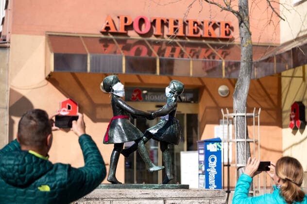 Unbekannte haben an die Statue zweier tanzender Mädchen im Zentrum von Jena Atemschutzmasken angebracht. Die Statue steht vor einer Apotheke. Zwei Passanten fotografieren die Statue. Foto vom 24.3.2020