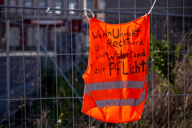 Warnweste 25.03.2020, Rheinland-Pfalz, Koblenz-Lützel: Auf einer orangenen Warnweste, die an einem Bauzaun befestigt ist, steht Wenn Unrecht zu Recht wird Widerstand zur Pflicht feeAssange.